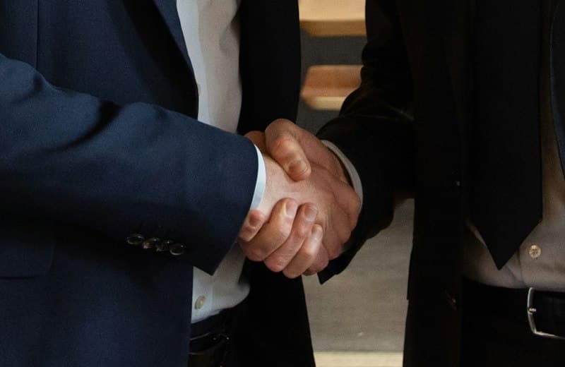 Dos personas de traje dándose la mano al cerrar un acuerdo