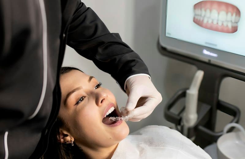 Dentista colocando un alineador transparente a una paciente, con el escaneo de su dentadura en el monitor